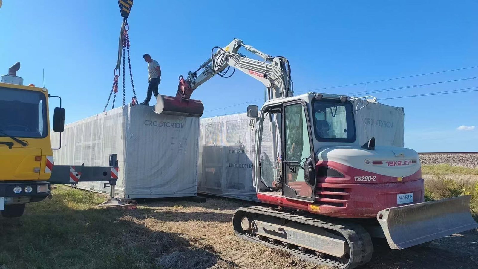 Grúa y excavadora trabajando junto a dos contenedores de baterías CROSTORION embalados en Vođinci